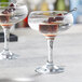 A pair of Pasabahce coupe glasses with liquid and cherries in them.