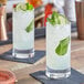 Two Nude Rocks long drink glasses filled with liquid and garnished with lime and mint leaves.