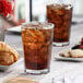 A Pasabahce Casablanca beverage glass filled with ice tea on a table with pastries.
