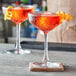 Two Pasabahce Timeless Vintage coupe glasses filled with red liquid and garnished with a spiral lemon peel.