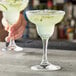 A hand holding a Pasabahce Capri margarita glass filled with a drink and garnished with a lime.