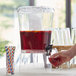 A hand pouring red liquid from a Choice acrylic beverage dispenser into a glass.