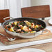 A Vigor stainless steel non-stick fry pan full of seafood and rice on a wooden cutting board.