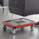 A person using a red and black CaterGator dolly to transport a black box.
