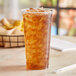 A 24 oz EcoChoice PLA compostable plastic cold cup filled with ice tea on a table.