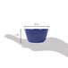 A hand holding a navy blue fluted ramekin with a table in the background.