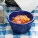 A navy blue fluted melamine ramekin filled with salsa on a table with a checkered tablecloth.