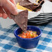 A person holding a chip and dipping it into a blue bowl of salsa.