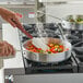 A person cooking food in a Choice aluminum saute pan on a stove.