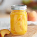 A Kerr pint canning jar filled with peaches on a wooden surface.