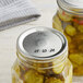 Two Kerr wide mouth canning jars of pickles on a kitchen counter with silver lids.
