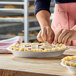 A person is preparing a pie with a crimped edge in a round metal pan on a wooden surface.