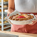 A person is holding a freshly baked pie in a round metal pan, using a cloth for protection.