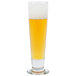 A Libbey tall footed pilsner glass filled with beer and foam.