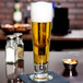 A customizable Libbey tall footed pilsner glass of beer on a table.
