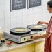 A dual non-stick crepe maker with two round cooking surfaces and control knobs, shown in use on a countertop.