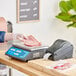 A person weighing meat on an AvaWeigh digital price computing scale on a counter in a deli with a black printer label.
