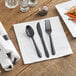 A white napkin with a black fork, spoon, and knife on it.