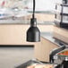 A ServIt ceiling mount heat lamp with a black dome shade over a buffet table of food.