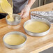 A person pouring yellow batter into a Choice round aluminum cake pan.