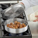A person cooking meatballs in a Choice aluminum saute pan on a stove.