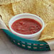 A basket of tortilla chips with bowls of Red Gold mild salsa on a table.