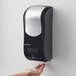 A hand using a black and silver San Jamar Summit Rely hybrid automatic foam soap and sanitizer dispenser.