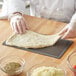 A person's hand rolling American Metalcraft Hard Coat Anodized Aluminum flatbread dough on a pizza screen.