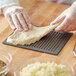 A person in gloves using an American Metalcraft Hard Coat Anodized Aluminum Mega Flatbread Screen to make pizza dough.