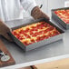 A person holding a Detroit-style pizza in an American Metalcraft hard coat anodized aluminum pan.