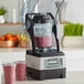 A Vitamix blending station with two cups of smoothies on the counter.