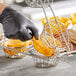 A person in black gloves uses a Choice Tortilla Fry Basket to put tortilla chips in small baskets.