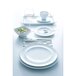 An Arcoroc white cup and saucer on a table with white plates and silverware.