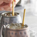 A person holding an Acopa gold stainless steel reusable straw in a copper mug with ice.