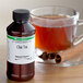 A bottle of LorAnn Oils All-Natural Chai Tea Super Strength Flavor next to a glass cup of tea.