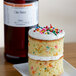 A cake with sprinkles on top and LorAnn Oils Cake Batter Flavor on a counter.