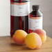 A bottle of LorAnn Oils Apricot Super Strength Flavor next to a group of peaches.