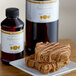 A bottle of LorAnn Oils Butterscotch Super Strength Flavor on a counter next to a plate of brown food.