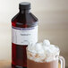 A cup of hot chocolate with marshmallows and a bottle of LorAnn Oils Marshmallow Super Strength Flavor syrup.