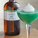 A glass with green liquid and a bottle of LorAnn Oils All-Natural Cool Creme de Menthe flavoring.