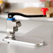 A Vollrath Redco EaziClean heavy duty can opener on a counter in a professional kitchen with a red handle.
