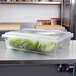 A Carlisle clear plastic food storage box filled with lettuce on a counter.