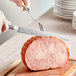 A person using a Choice stainless steel serrated knife to cut a piece of meat.