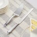 A Choice stainless steel cake serving set with a knife and cake server on a table with a cake.