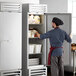 A man in a hat and apron opens the white solid door of a Beverage-Air reach-in refrigerator.