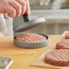A person using a Choice cast aluminum hamburger press with a wooden handle to press hamburger patties.