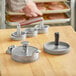 A man uses a Choice hamburger press with a wooden handle to make hamburger patties.