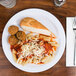 A white Carlisle melamine plate with pasta, meatballs, and bread.