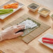 A person's hand using an Emperor's Select bamboo sushi mat to roll sushi.