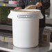 A large white round ingredient storage bin labeled 'Baker's Mark' with a person scooping contents from it.